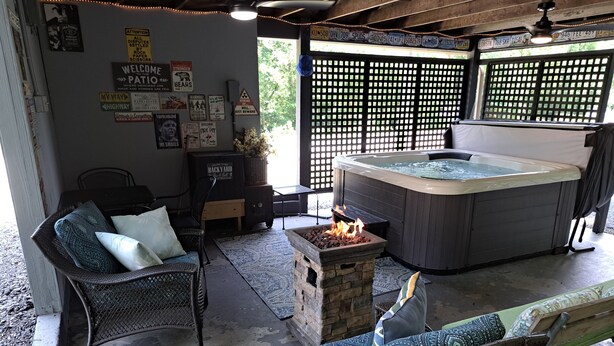Area patio con vasca idromassaggio, mobili in vimini e un elemento decorativo con fuoco.