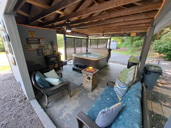 A covered outdoor seating area with a fire feature, wicker furniture, and a hot tub.