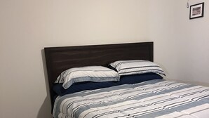 A single bed with a dark headboard, a striped bedspread, and a single wall-mounted light fixture. - A lovely and well spaced one bedroom with a pool view (Houston)