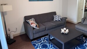 A modern living room with a grey sofa, patterned cushions, a black coffee table, and a cityscape painting on the wall. - A lovely and well spaced one bedroom with a pool view (Houston)