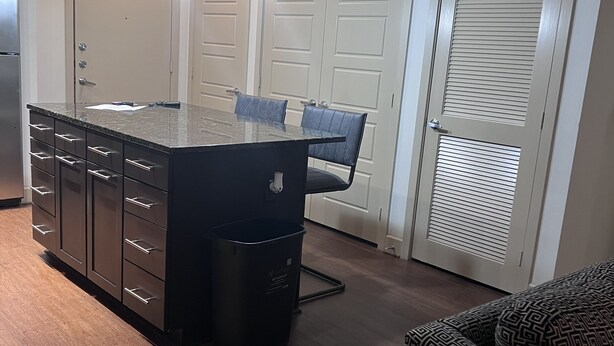 A modern kitchen with a central island, pendant lighting, and a dining area with chairs. - A lovely and well spaced one bedroom with a pool view (Houston)