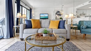 A modern living room with a grey sofa, yellow cushions, a glass coffee table, and a TV on a stand. - ~Gorgeous~ Ocean View King Suite in Cabana Row~ (Myrtle Beach)
