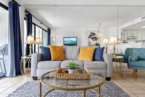 A modern living room with a grey sofa, yellow cushions, a glass coffee table, and a TV on a stand. - ~Gorgeous~ Ocean View King Suite in Cabana Row~ (Myrtle Beach)
