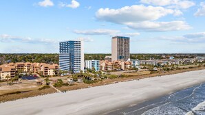 A coastal hotel area with beachfront properties, including a tall blue building and a shorter beige building, with a sandy beach and ocean in the foreground. - ~Gorgeous~ Ocean View King Suite in Cabana Row~ (Myrtle Beach)