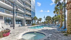 A pool area with two hot tubs, lounge chairs, and a building with balconies. - ~Gorgeous~ Ocean View King Suite in Cabana Row~ (Myrtle Beach)