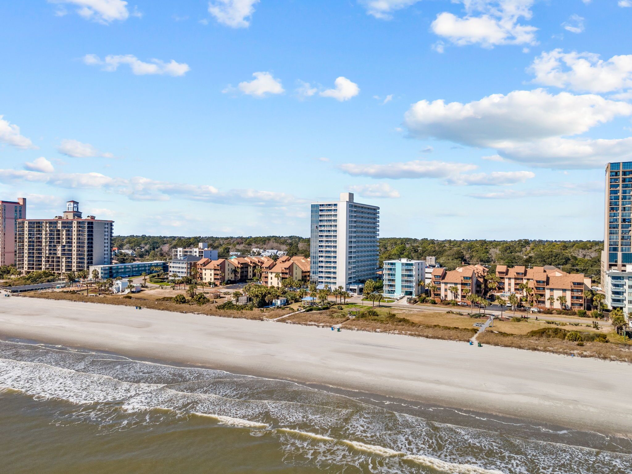 Un paysage urbain côtier avec de hauts immeubles, une plage de sable et un ciel dégagé.