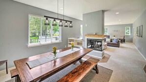 A spacious living area with a large wooden dining table, a fireplace, and a view of the outdoors through large windows. - Riverside North Bend Oasis: Stunning Mountain View (North Bend)