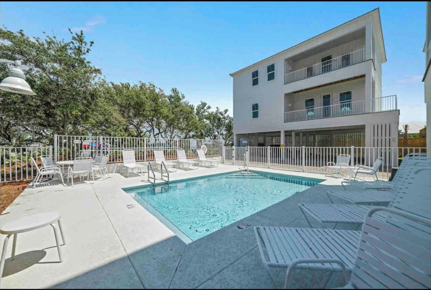 Un bâtiment moderne doté d’une piscine, entouré de chaises blanches et d’une clôture.