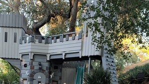 A castle-like structure with a slide, stone steps, and a chain-link fence. - A Taste of Tuscany -Just 5 Minutes to Golf and Wine Tasting  (Fallbrook)