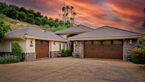 A two-story house with a stone facade, a garage with a large wooden door, and a driveway. - A Taste of Tuscany -Just 5 Minutes to Golf and Wine Tasting  (Fallbrook)