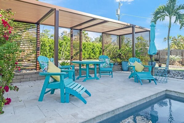 A covered outdoor seating area with turquoise chairs and a pool.