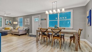 A spacious living room with a dining area, hardwood floors, and a large window with blue shutters. - Coastal Soul House in the heart of Naples (Naples)