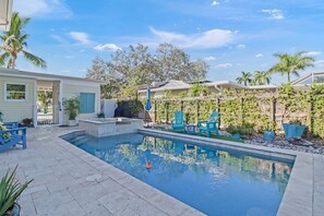 A swimming pool with a small hot tub, surrounded by a patio area with blue chairs and a covered seating area.