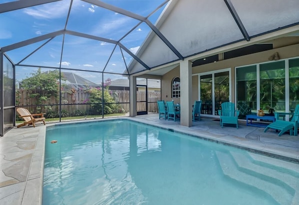 A covered outdoor swimming pool with a glass ceiling, surrounded by turquoise chairs and a wooden deck. - Cozy Beach House - 5 minutes from Vanderbilt Beach (Naples)
