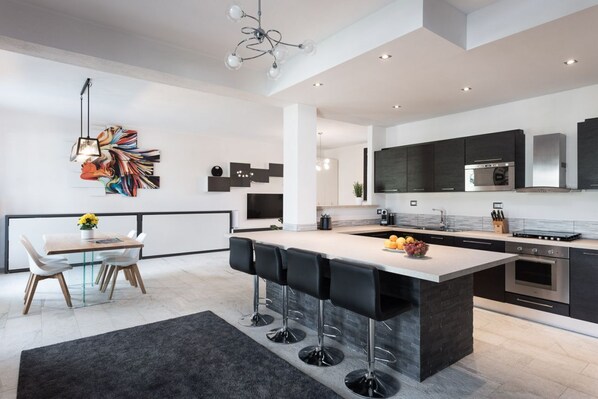 Una cocina moderna con una isla central, taburetes de bar y un comedor con mesa y sillas.