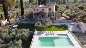 Eine mediterrane Villa mit Schwimmbad, umgeben von Olivenhainen und Zypressen.