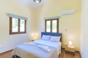 Quarto com cama, duas mesas de cabeceira com luminárias, ar condicionado e janelas com persianas.
