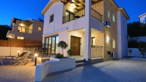 A modern two-story house with a balcony, outdoor seating, and a well-lit entrance.