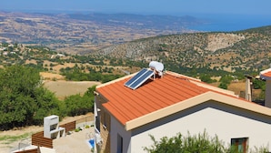 A modern building with a red roof, solar panels, and a view of a hilly landscape.