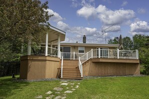 A two-story house with a covered porch, a staircase, and a deck with outdoor furniture.