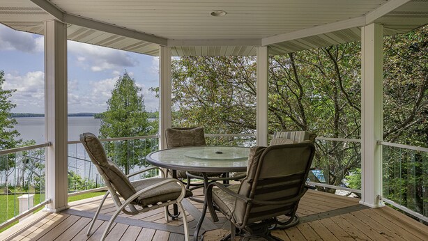 A covered outdoor area with a table and chairs, overlooking a body of water and trees.