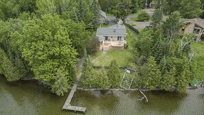 An aerial view of a lakeside house with a dock, surrounded by dense trees.