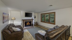 A living room with a fireplace, leather sofas, a TV, and a window with a view of trees.