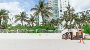 A beachfront hotel with a white fence, palm trees, and a high-rise building in the background. - Apt w/2 Queen Beds and Canal View at Tides (Hollywood)