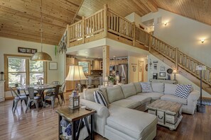 Ein geräumiger Wohnbereich mit hoher Decke, einer Holztreppe und einem Essbereich mit modernen Möbeln.