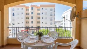 Un balcone con un tavolo apparecchiato per quattro persone, sedie bianche di plastica e vista su un edificio a più piani.