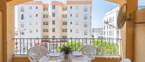 A balcony with a table set for four, white plastic chairs, and a view of a multi-story building.