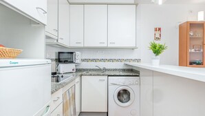 Una cucina funzionale con mobili bianchi, un forno a microonde, un tostapane, un lavello e una lavatrice.