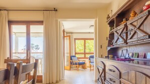 Ein geräumiges Zimmer mit einem Holzespeisebereich, Stühlen, einer Küchenzeile mit Holzschränken und Blick durch ein großes Fenster.