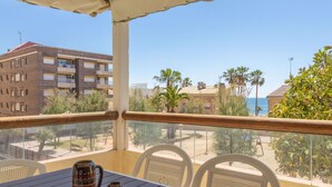 Ein Balkon mit Tisch und Stühlen mit Blick auf einen Strand und Gebäude.