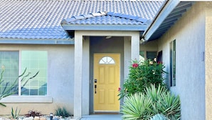 A house with a tiled roof, a yellow front door, and a concrete pathway leading to the entrance. - ★Hot tub under the stars★ 4-King Beds, Cowboy Pool, Game Room, Fire Pit, JTNP (Twentynine Palms)
