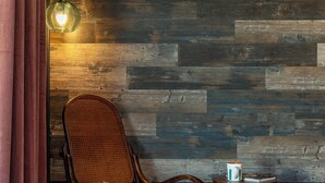 A room with a wooden wall, a rocking chair, a small wooden table with a mug, and a fluffy rug. - ★Hot tub under the stars★ 4-King Beds, Cowboy Pool, Game Room, Fire Pit, JTNP (Twentynine Palms)