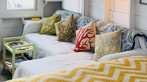 Quarto aconchegante com cama, uma mesinha, abajur e janela com vista.