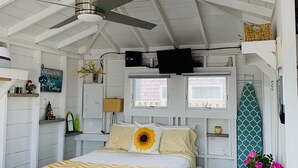 Quarto com cama, ventilador de teto, uma prancha de surf e janela.
