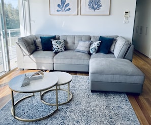Ein modernes Wohnzimmer mit einem grauen Ecksofa, zwei runden Couchtischen und einem gemusterten Teppich.