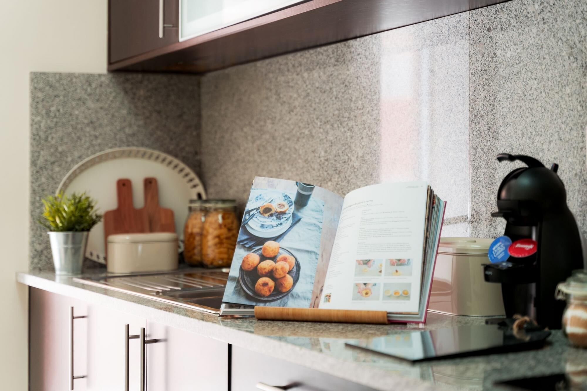 A kitchen counter with a cookbook, a coffee machine, and a jar of spices.