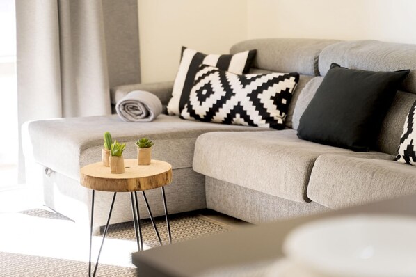 A modern living room with a grey sofa, black and white patterned pillows, and small potted plants on a wooden side table.
