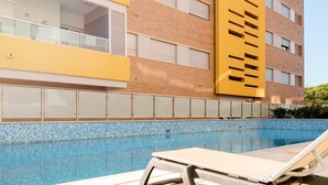 A modern building with a swimming pool, a yellow facade, and a glass balustrade. - T1 Varandas Forte Piscina Ar Cond Garagem (Loulé)