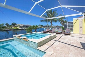 Ein Poolbereich mit freiem Blick auf das Wasser, Liegestühle und eine überdachte Terrasse.