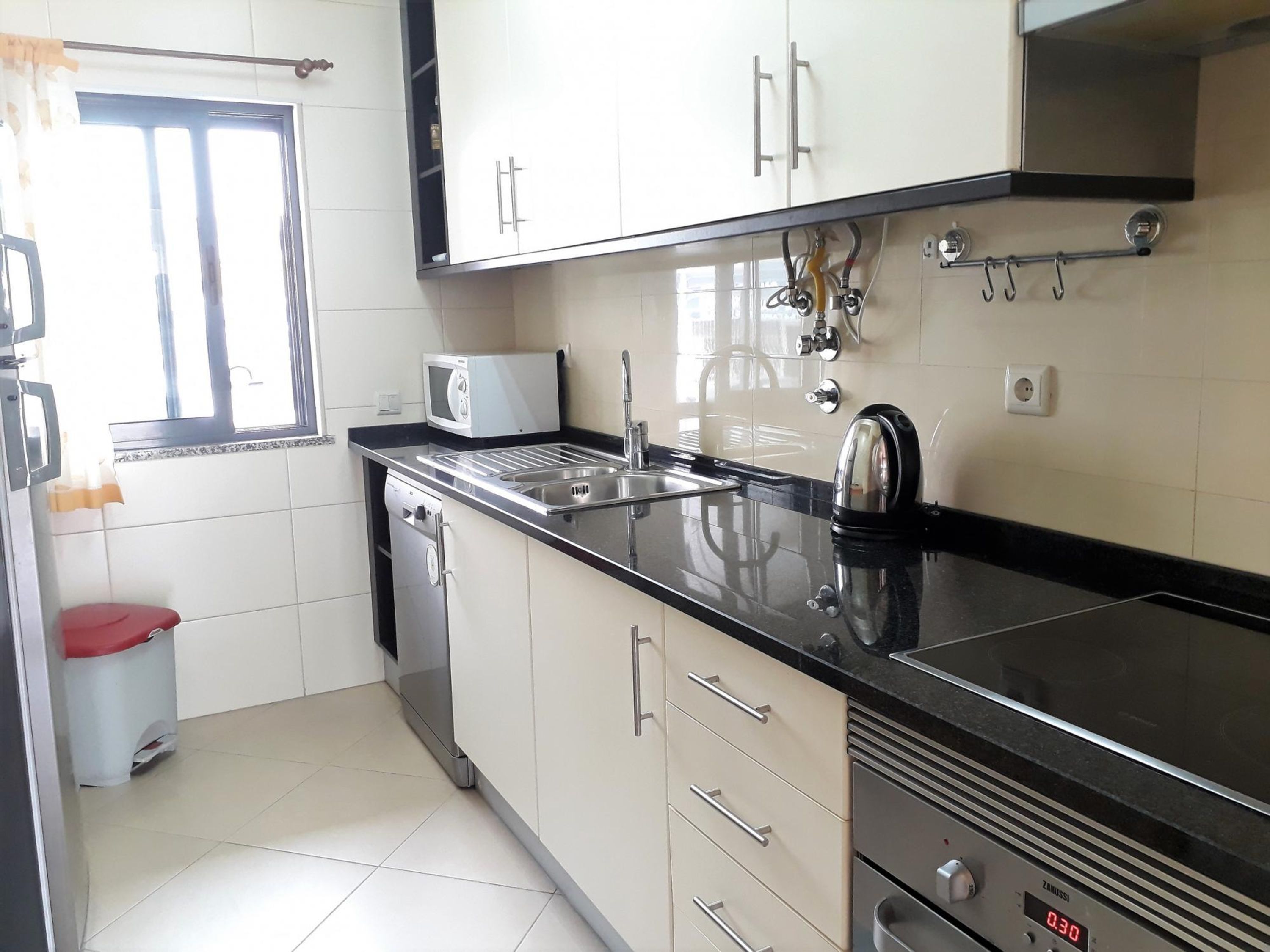 A kitchen with a microwave, kettle, sink, and a dishwasher.