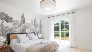 A bedroom with a large bed, a nightstand, a lamp, and a mural of trees on the wall.