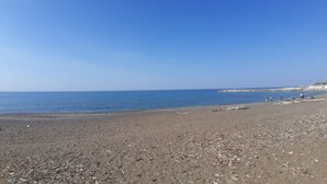 En strand med klart skys og roligt hav, med et par mennesker i det fjerne.