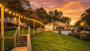A wooden deck with a staircase leading to a covered area, surrounded by a well-maintained lawn and trees. - Your adventure at the Lake. 9 Mi from the Ark Encounter, breathtaking view. (Dry Ridge)
