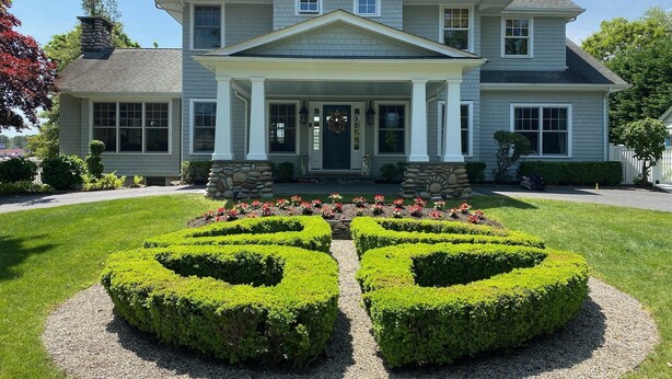 A two-story house with a front porch, stone pillars, and a symmetrical garden with hedges. - Spectacular Riverfront Property (Manasquan)