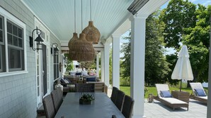 A covered patio with a dining table and chairs, a wicker sofa, and a lounge area with chairs and an umbrella. - Spectacular Riverfront Property (Manasquan)