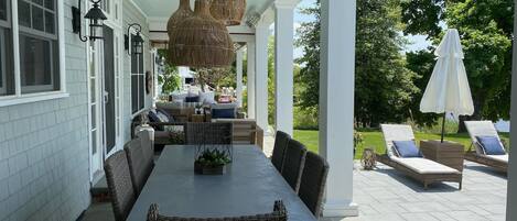 A covered patio with a dining table and chairs, a wicker sofa, and a lounge area with chairs and an umbrella.
